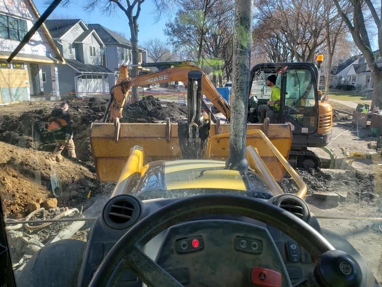 From a vehicle's dashboard, excavators and workers dig near houses under construction.