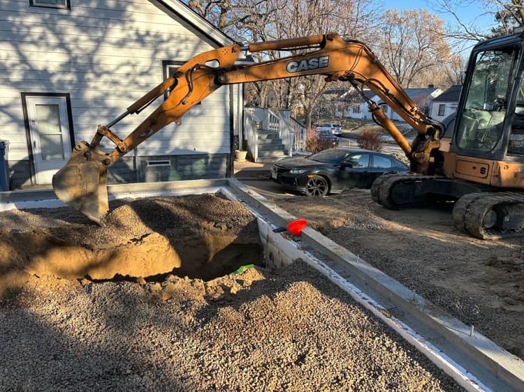 CASE excavator digging a foundation trench next to a house and parked car.